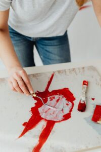 A focused artist uses a palette knife to create red abstract art on canvas.