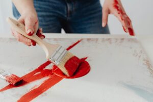 Artist's hand applying red paint on canvas with a brush in a creative setting.